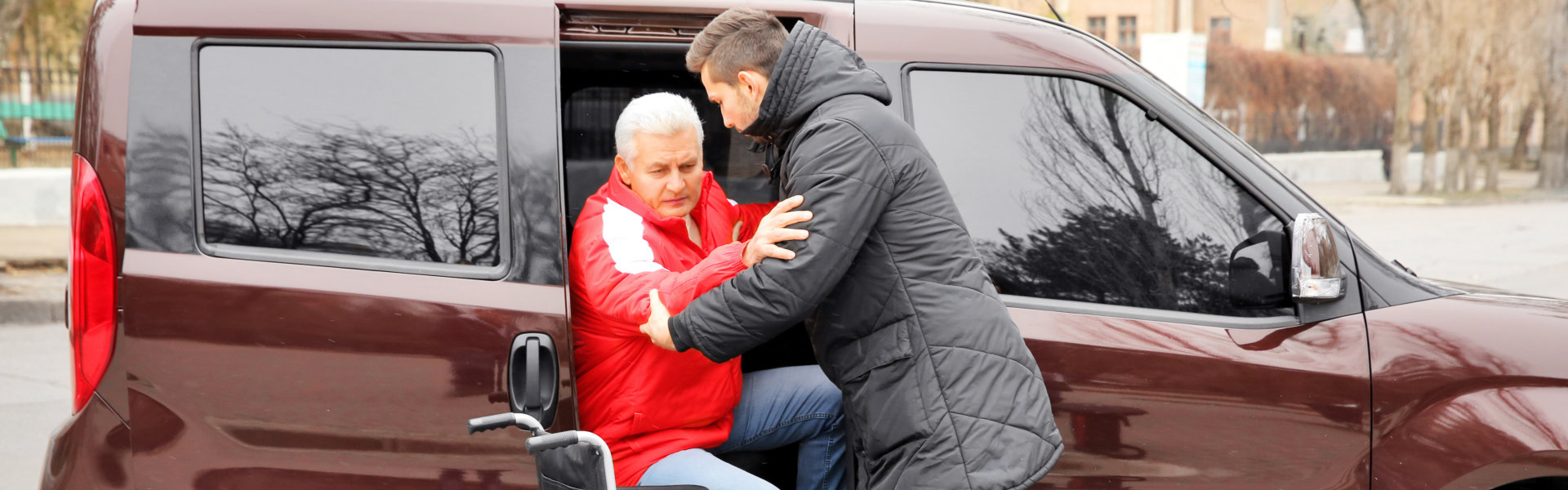 Young man helping handicapped man to sit in wheelchair