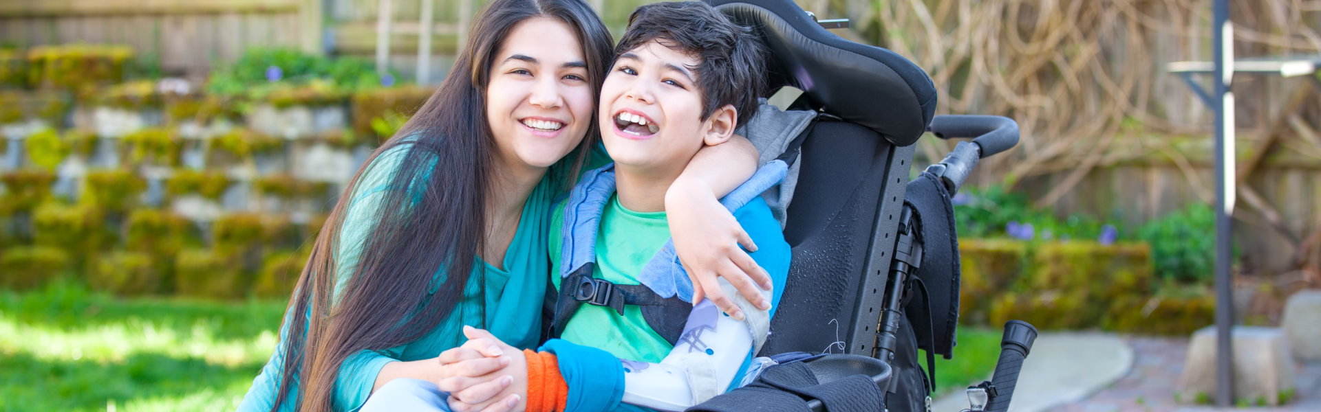 Teenage girl hugging brother in wheelchair outdoors
